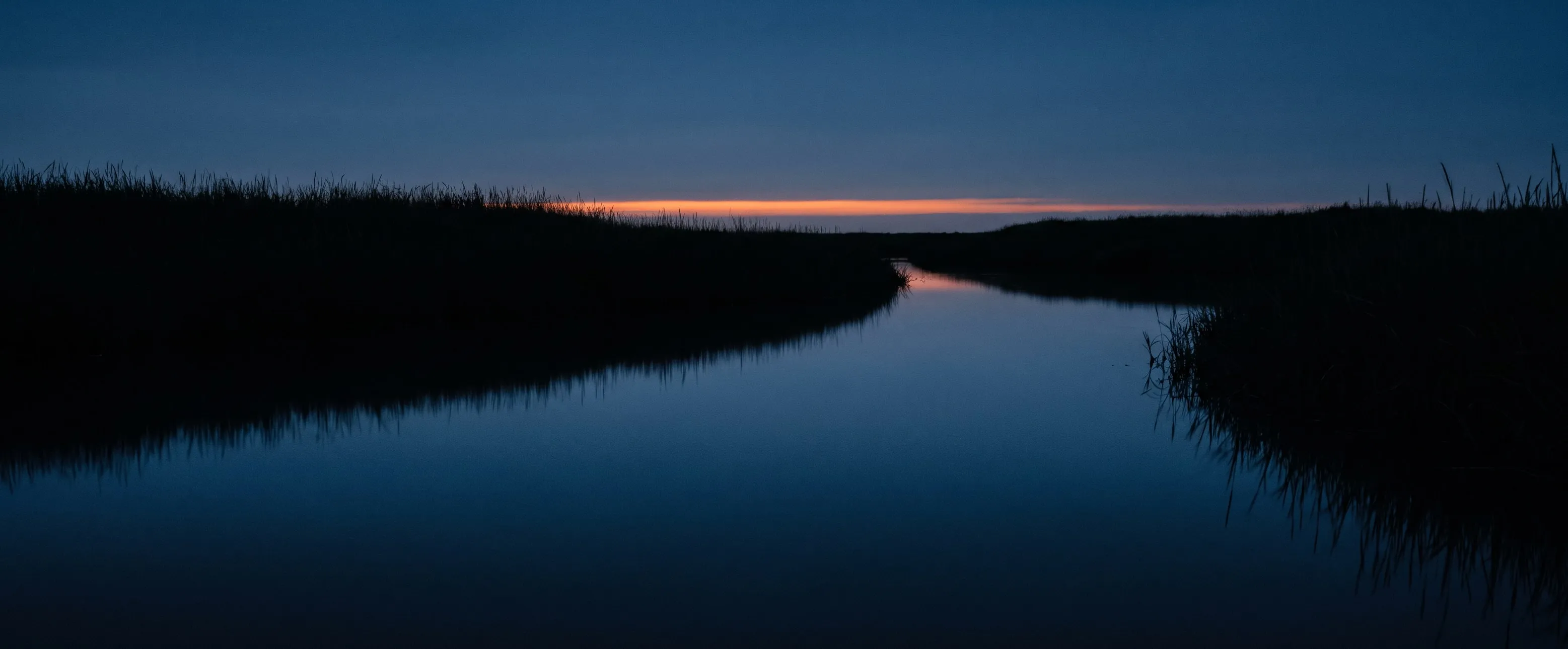 Ein Priel bei Dämmerung, stilles Wasser spiegelt den letzten Lichtstreifen