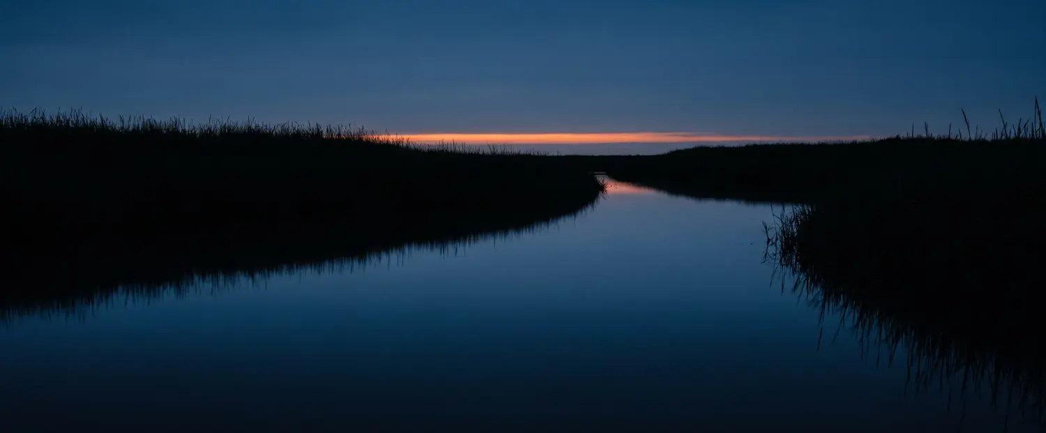 Ein Priel bei Dämmerung, stilles Wasser spiegelt den letzten Lichtstreifen
